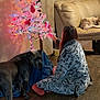 person, dog, christmas_tree, lights, ornaments, couch, robe, floor, indoor, wooden_floor, curtains, decor, pet, holiday, relaxing, seated, sleeping_dog, furniture, home, cozy