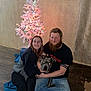 Tennessee is registered to the contest to win money with this photo: couple, dog, indoor, christmas_tree, lights, floor, wooden_floor, deer_head_mount, beard, casual_clothing, smile, hugging, flash_reflection, legs, wall, curtains, calendar, tattoo, footwear, jeans