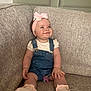Nola is registered to the contest to win money with this photo: baby, child, smile, headband, bow, denim_overalls, pacifier, socks, couch, furniture, indoor, person, happy, cute, infant, portrait, sitting, clothing, skin, young