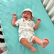 Claudius is registered to the contest to win money with this photo: baby, blue_sheet, child, crib, cute, expression, foot, hand, happy, hat, indoors, infant, joy, newborn, person, playful, romper, sleepwear, smiling, white_crib