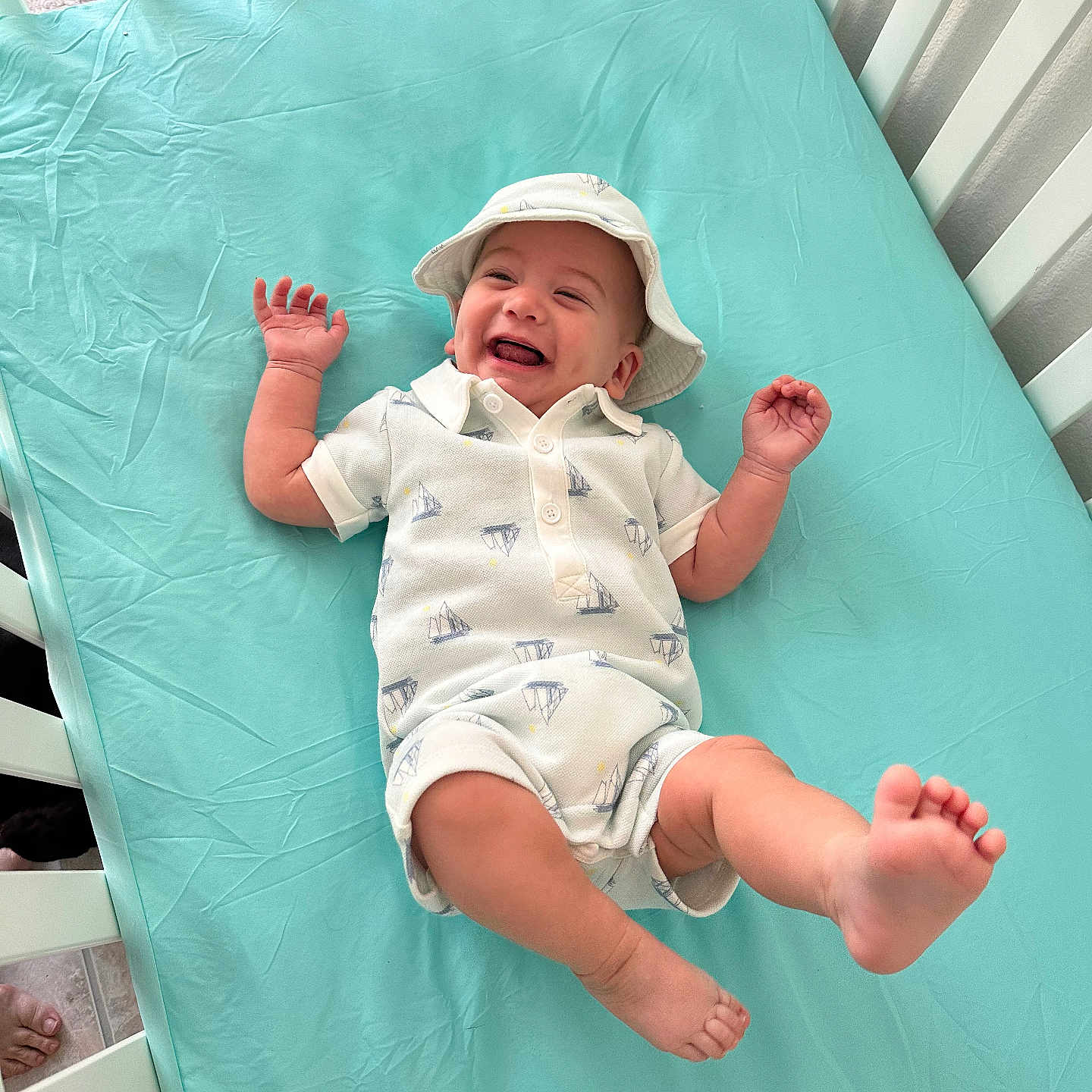 Claudius is registered to the contest to win money with this photo: baby, blue_sheet, child, crib, cute, expression, foot, hand, happy, hat, indoors, infant, joy, newborn, person, playful, romper, sleepwear, smiling, white_crib