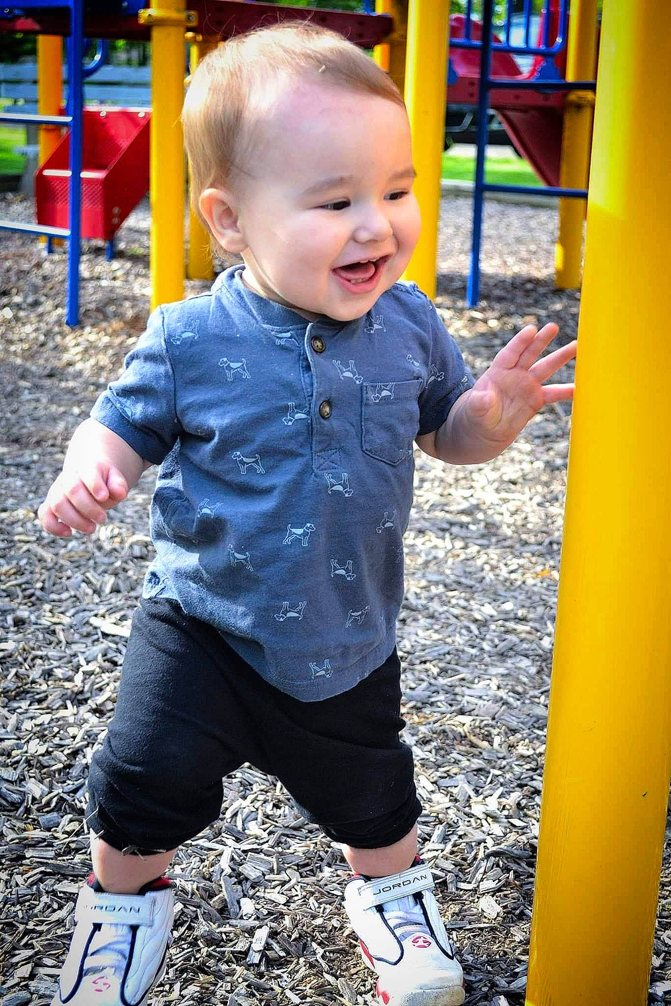 Zayden is registered to the contest to win money with this photo: baby_toddler_clothing, black, blue, facial_expression, fun, happy, leisure, light, organ, person, photograph, playground, product, red, sleeve, smile, sneakers, standing, toddler, white