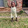 brick_wall, celebration, child, dress, grass, greenery, happy, nature, outdoor, person, plant, portrait, sandals, smiling, standing, summer, sunflowers, toddler, window, yard