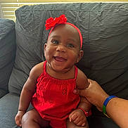 Milena is registered to the contest to win money with this photo: accessory, baby, child, couch, cute, flower, furniture, hand, happy, headband, indoor, infant, person, portrait, red_dress, sitting, skin, smile, window_blinds, wristband
