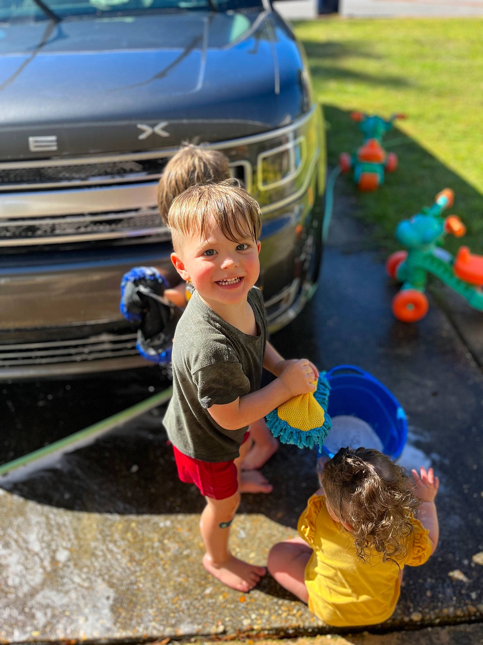 Phoenix is registered to the contest to win money with this photo: automotive_design, automotive_exterior, automotive_lighting, blue, bumper, car, child, fun, grass, green, grille, hood, joy, leisure, light, motor_vehicle, person, personal_luxury_car, shorts, toddler
