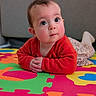 baby, child, red_sweater, colorful_mat, puzzle_mat, floor_play, curious_expression, rosy_cheeks, big_eyes, long_eyelashes, floral_skirt, white_socks, indoors, soft_lighting, portrait, closeup, infant, hands_folded, cute, playtime