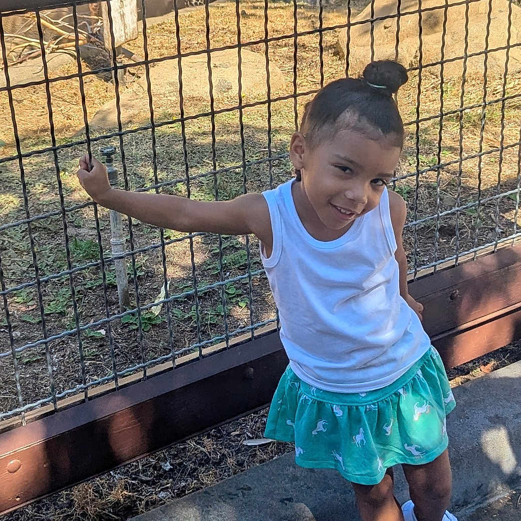 Cali joined the competition — help win amazing prizes! animal, child, clothing, face, fence, footwear, grass, head, nature, outdoors, park, person, photography, plant, portrait, shoe, shorts, skirt, tree, zoo