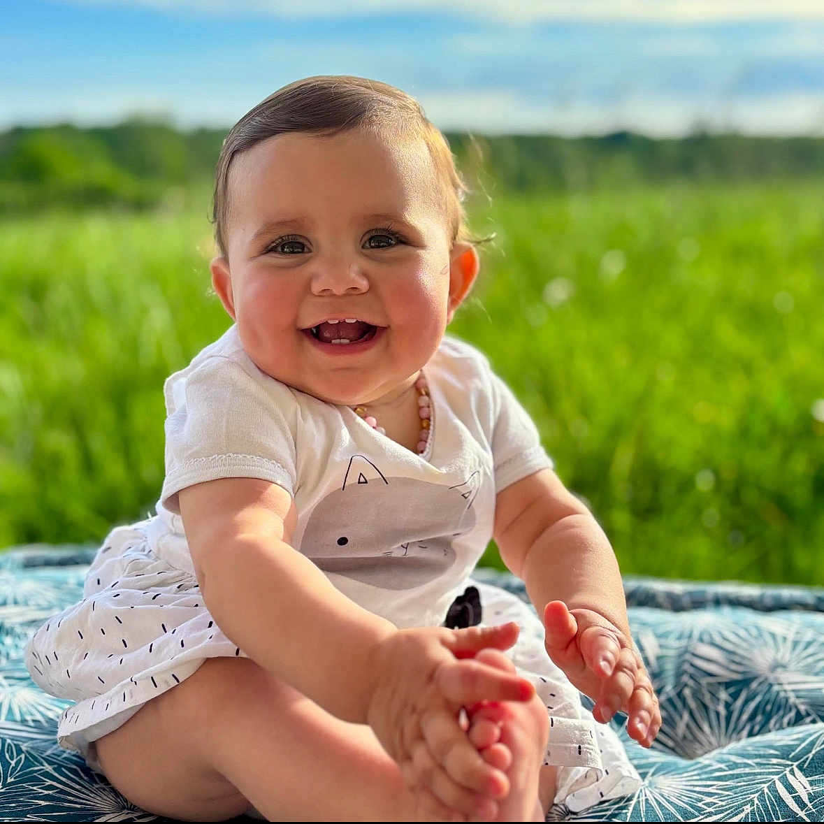 Zelya participe au concours pour gagner de l'argent avec cette photo : baby, blanket, child, cute, daylight, face, grass, greenery, happy, infant, nature, outdoor, person, playful, portrait, sitting, smiling, sunlight, toes, white_clothing