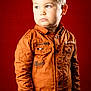 Arthur participe au concours pour gagner de l'argent avec cette photo : boy, buttoned_shirt, casual_clothes, child, cute, ear, eye, fashion, hands_in_pockets, innocent, looking_away, orange_shirt, portrait, red_background, serious_expression, short_hair, standing, studio, studio_lighting, young_child