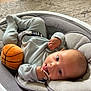baby, infant, pacifier, toy, basketball, baby_rocker, gray, carpet, wood_floor, indoor, clothing, cute, child, person, relaxing, soft_toy, small_hand, head, face, lying_down