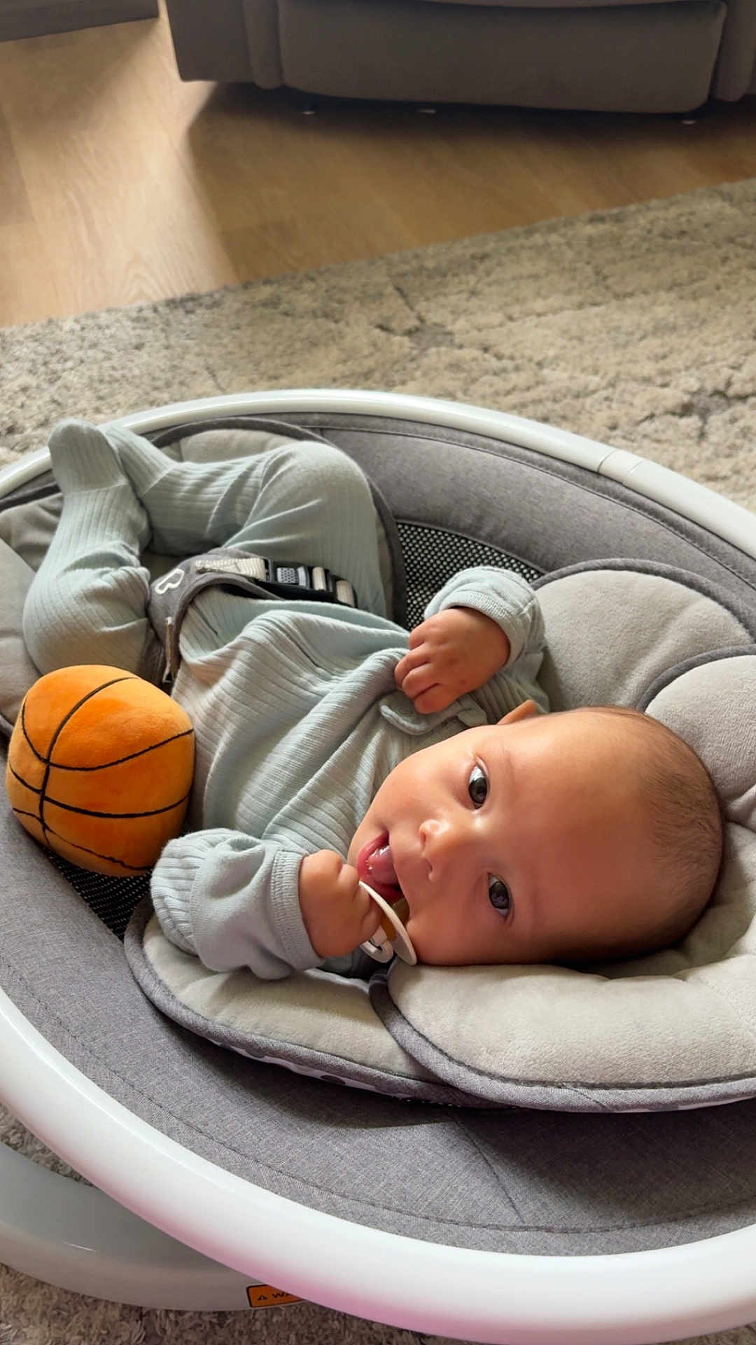 Bryson joined the competition — help win amazing prizes! baby, infant, pacifier, toy, basketball, baby_rocker, gray, carpet, wood_floor, indoor, clothing, cute, child, person, relaxing, soft_toy, small_hand, head, face, lying_down