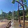 children, water_play, splash_pad, outdoor, summer, playground, water_splash, kids, fun, sunny_day, greenery, trees, blue_sky, play_equipment, water_bucket, wet, active, joyful, recreation, park