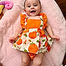 Solena is registered to the contest to win money with this photo: arms, baby, child, cute, dress, eyes, face, floor, happy, indoors, infant, laying_down, legs, orange, patterned_clothing, pink_blanket, playful, plush_toy, smile, soft_texture