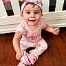 baby, bunny_ears, child, crib, cute, floral_pants, girl, happy, headband, headwear, indoors, person, pink_clothing, portrait, sitting, slippers, smiling, white_furniture, wooden_floor, young_child