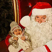 Séréna participe au concours pour gagner de l'argent avec cette photo : baby, child, santa_claus, christmas, holiday, hat, beard, glasses, red_clothing, white_gloves, chair, smile, festive, winter_clothing, tree, cozy, portrait, indoor, happy, person