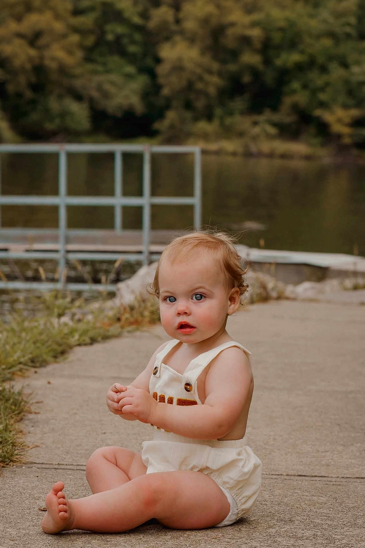 Kylo joined the competition — help win amazing prizes! toddler, child, baby, outdoor, lake, water, concrete_path, grass, trees, greenery, romper, sitting, barefoot, curious, nature, summer, portrait, young_child, daylight, casual_clothing