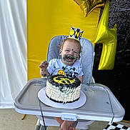 Kylo joined the competition — help win amazing prizes! baby, birthday, cake, high_chair, crown, smiling, messy, face_paint, balloons, yellow, black, celebration, first_birthday, party, child, happy, food, indoor, clothing, flag