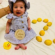 Eileen is registered to the contest to win money with this photo: baby, infant, two_months, purple_dress, hat, yellow_lemons, rubber_duck, hand, white_sheet, smiling, sitting, cute, child, portrait, indoors, bright, happy, playful, decor, person