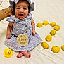 baby, infant, two_months, purple_dress, hat, yellow_lemons, rubber_duck, hand, white_sheet, smiling, sitting, cute, child, portrait, indoors, bright, happy, playful, decor, person