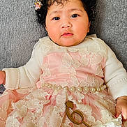 Devira is registered to the contest to win money with this photo: baby, curly_hair, flower_crown, pink_dress, lace, pearl_belt, couch, gray_background, infant, portrait, cute, indoors, child, soft_lighting, fashion, hand, expression, sitting, closeup, person