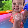 child, toddler, smiling, happy, swimming, pool, kiddie_pool, water, swimsuit, outdoor, summer, grass, trampoline, portrait, close_up, wet, teeth, fist, colorful, playtime