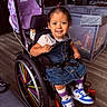 child, colorful, denim_dress, family, girl, happy, home, indoors, playpen, playroom, portrait, rainbow, seated, smiling, sneakers, striped_shirt, stroller, toddler, wheel, wheelchair