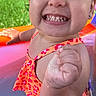 toddler, child, smiling, grinning, outdoor, pool, swimsuit, summer, sunlight, portrait, face, teeth, raised_fist, happy, playful, water, colorful, greenery, close_up, smartphone_screenshot