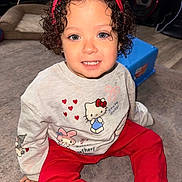 Mazikeen is registered to the contest to win money with this photo: toddler, child, curly_hair, smiling, portrait, indoor, sitting, carpet, red_bow, headband, pajamas, hello_kitty, red_pants, toy, pet_bed, speakers, living_room, flash_photography, happy, fashion