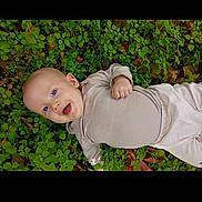 Vincent is registered to the contest to win money with this photo: baby, infant, smiling, happy, blue_eyes, lying_down, greenery, leaves, nature, outdoor, clothing, beige_outfit, cute, child, person, skin, head, hand, baby_girl, baby_boy