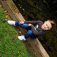 Furious is registered to the contest to win money with this photo: child, boy, grass, concrete, water, rocks, leaves, jeans, sneakers, long_sleeve_shirt, outdoor, nature, casual_clothing, park, sitting, smile, daylight, young, sidewalk, relaxing