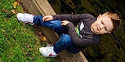 Furious is registered to the contest to win money with this photo: child, boy, grass, concrete, water, rocks, leaves, jeans, sneakers, long_sleeve_shirt, outdoor, nature, casual_clothing, park, sitting, smile, daylight, young, sidewalk, relaxing