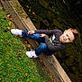 child, boy, grass, concrete, water, rocks, leaves, jeans, sneakers, long_sleeve_shirt, outdoor, nature, casual_clothing, park, sitting, smile, daylight, young, sidewalk, relaxing