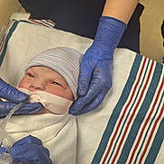 Gabriella joined the competition — help win amazing prizes! newborn, baby, hospital, medical, gloves, breathing_tube, blanket, infant, person, healthcare, bed, striped_cap, care, hands, closeup, patient, medical_equipment, swaddled, clinic, newborn_care