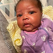 Terriana is registered to the contest to win money with this photo: baby, infant, close_up, face, purple_clothing, knitted_blanket, yellow_blanket, patterned_fabric, newborn, cute, soft_texture, sleepwear, portrait, young_child, indoors, cozy, expression, small_hands, skin, eyes