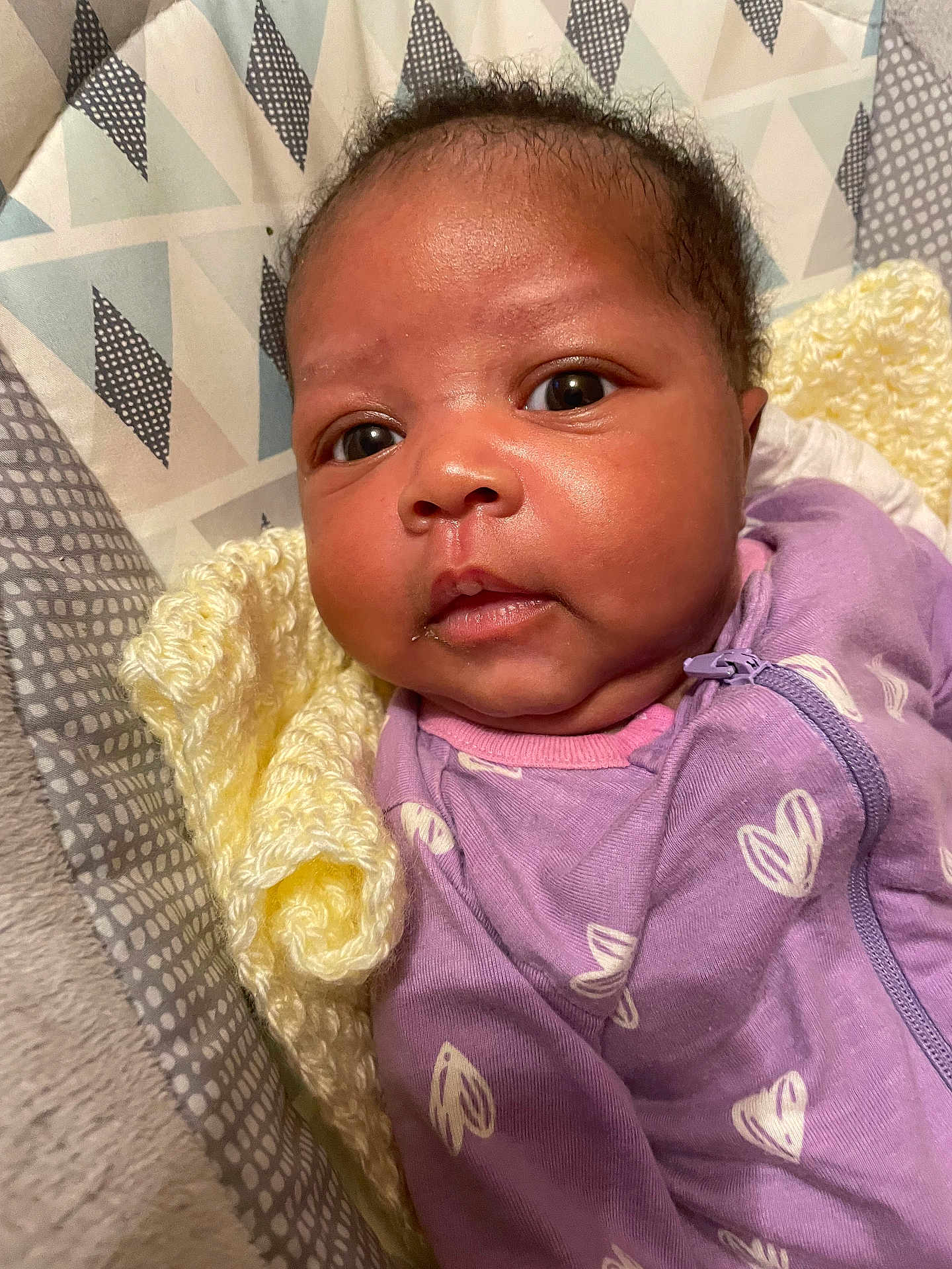 Terriana is registered to the contest to win money with this photo: baby, infant, close_up, face, purple_clothing, knitted_blanket, yellow_blanket, patterned_fabric, newborn, cute, soft_texture, sleepwear, portrait, young_child, indoors, cozy, expression, small_hands, skin, eyes