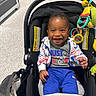 baby, smiling, stroller, toy, hoodie, blue_pants, indoor, child, happy, infant, face, clothing, seat, person, playful, cute, young_child, casual, portrait, dangle