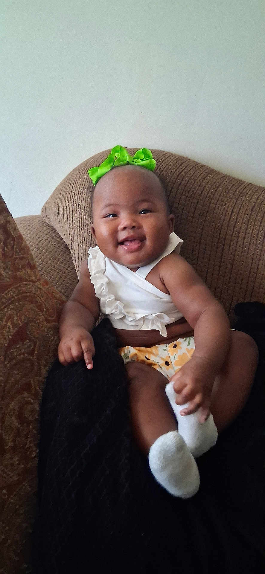 Jilisha joined the competition — help win amazing prizes! baby, child, smiling, green_bow, white_top, floral_bottoms, socks, brown_chair, happy, cute, indoors, infant, portrait, person, seated, cozy, comfortable, tongue_out, playful, young