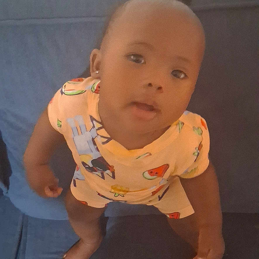 Jilisha joined the competition — help win amazing prizes! barefoot, blue, child, colorful_clothing, couch, curious, expression, furniture, head, home, indoors, looking_up, person, playful, portrait, short_sleeves, skin, standing, toddler, young_child