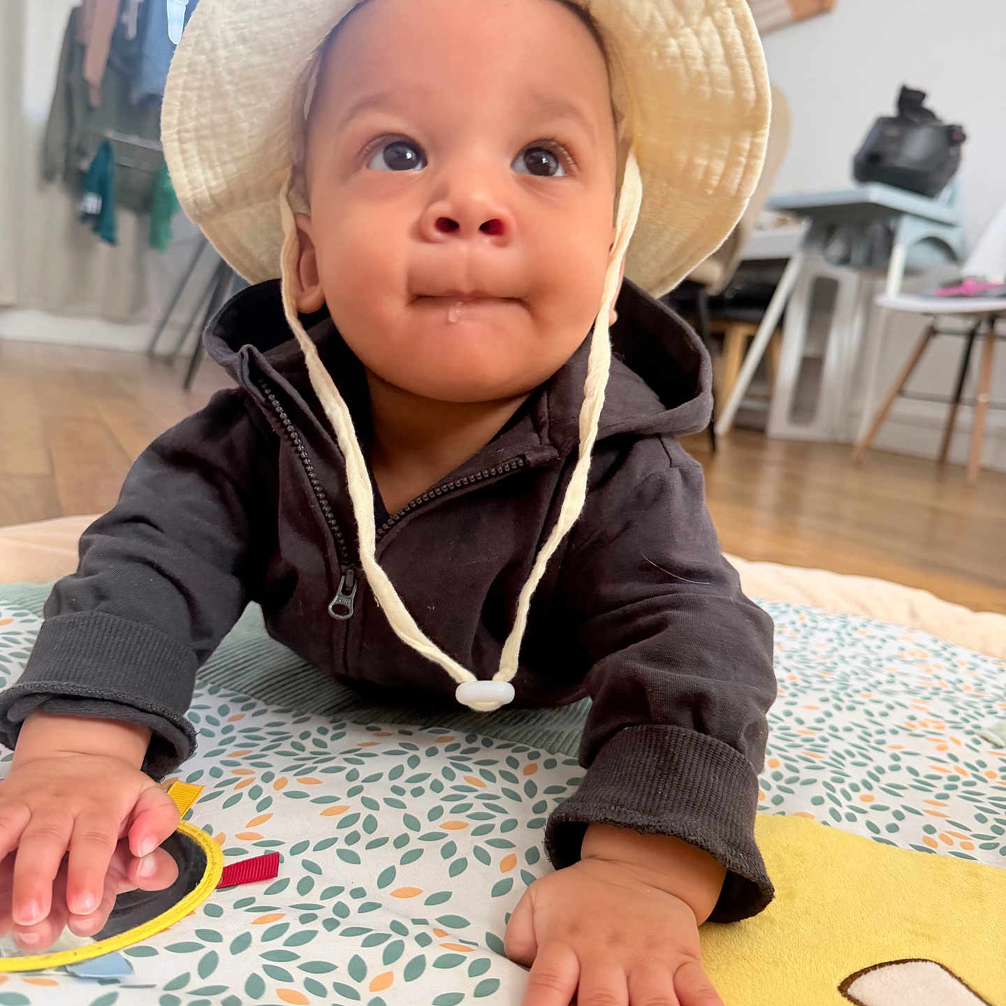 Elhan a rejoint le concours — aidez-le/la à gagner de superbes lots ! baby, big_eyes, bucket_hat, child, close_up, crawling, curious, cute, drool, face, hands, hat, home, hoodie, indoor, infant, playmat, portrait, toy, wooden_floor