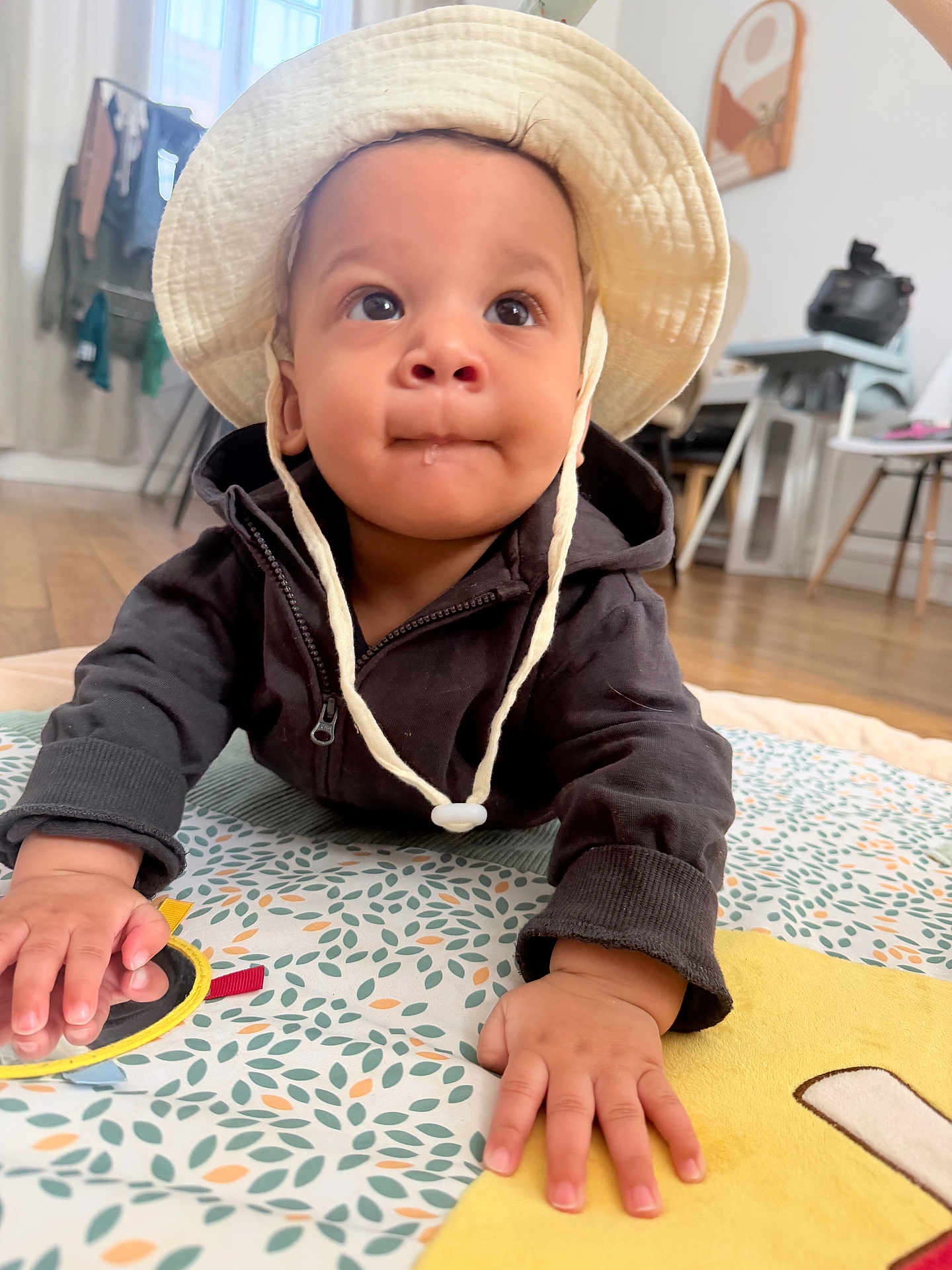 Elhan a rejoint le concours — aidez-le/la à gagner de superbes lots ! baby, infant, child, hat, bucket_hat, crawling, playmat, hands, face, big_eyes, drool, hoodie, indoor, wooden_floor, toy, close_up, portrait, curious, home, cute