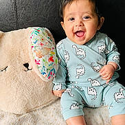 Meera joined the competition — help win amazing prizes! baby, smile, dinosaur_print, onesie, stuffed_animal, fluffy, toy, face, happy, child, infant, foot, hand, seated, fabric, cushion, home, indoor, cute, portrait
