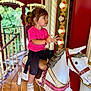 toddler, child, carousel, horse, ride, amusement_park, pink_shirt, white_horse, smiling, fun, playful, outdoor, wooden_floor, lights, decorative, hair_tied, sneakers, seatbelt, holding_pole, portrait
