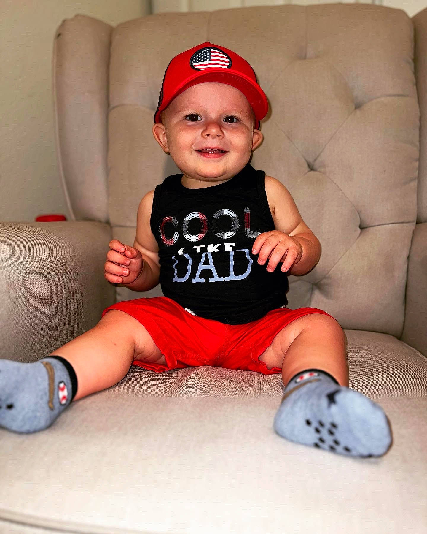 Maddax is registered to the contest to win money with this photo: baby, baby_toddler_clothing, baseball_cap, cap, carmine, comfort, costume_hat, elbow, happy, headwear, human_leg, joy, knee, lap, leg, person, shorts, sitting, sleeve, smile