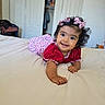 baby, child, girl, smiling, bed, pink_bows, red_dress, floral_pattern, indoor, portrait, happy, cute, person, infant, hair_bows, lying_down, bedroom, home, skin, face