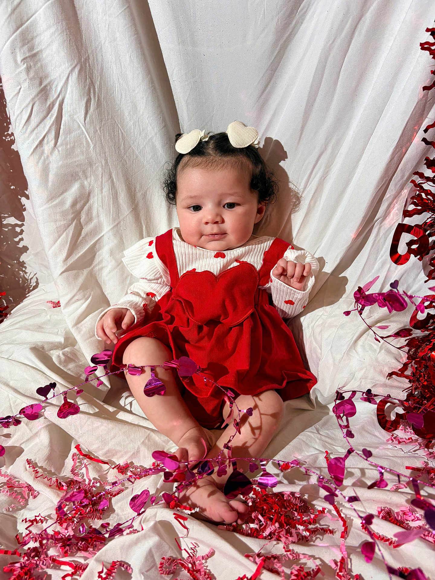 Avaya joined the competition — help win amazing prizes! baby, child, infant, red_dress, heart_clips, curly_hair, pink_decorations, red_decorations, white_backdrop, sitting, barefoot, cute, festive, celebration, portrait, adorable, indoors, holiday_theme, smiling, young