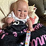 baby, smile, blanket, unicorn, plush_toy, couch, person, indoors, child, face, hand, expression, cozy, clothing, colorful, ribbon, furniture, home, cute, portrait