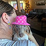 dog, puppy, pink_hat, polka_dots, person, ear, face, eyes, nose, close_up, portrait, indoor, living_room, christmas_tree, bokeh_lights, couch, holding, earring, shirt, cute
