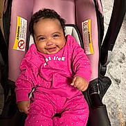 Janiya joined the competition — help win amazing prizes! baby, child, infant, smiling, happy, portrait, car_seat, pink_clothing, polka_dots, curly_hair, sitting, indoor, transportation, safety_seat, baby_clothes, face, hands, wood_floor, vehicle, photography