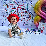 Gemma is registered to the contest to win money with this photo: abstract_art, artistic, balloon, black_and_white_dress, canvas, child, colorful_paint, creative, festive, happy, indoors, number_8, paint_brushes, paint_pots, portrait, red_beret, sitting, smiling, toddler, white_blanket