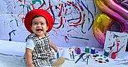 Gemma is registered to the contest to win money with this photo: toddler, child, red_beret, black_and_white_dress, white_blanket, paint_brushes, paint_pots, canvas, abstract_art, colorful_paint, balloon, number_8, smiling, happy, sitting, indoors, creative, artistic, festive, portrait